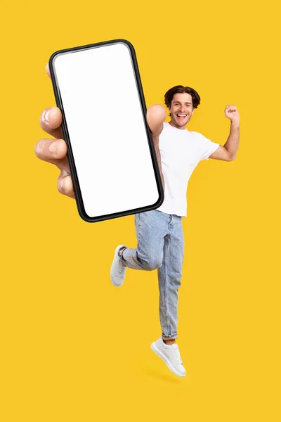 Mann zeigt weißen leeren Smartphone-Bildschirm und springt hoch — Stockfoto