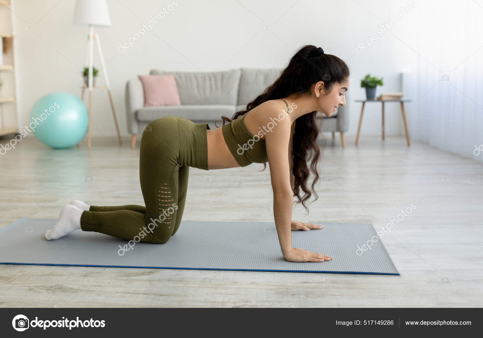 Sidovy av ung indisk dam gör övningar för sin ryggrad hälsa, stående i ko  yoga pose hemma, full längd — stockfoto © Milkos #517149286, image size:1600x1122