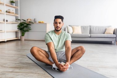 Ev antrenmanı. Spor yapan genç bir Arap, oturma odasında mindere uzanmış yoga yapıyor.