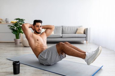 Çıplak gövdeli yakışıklı bir Arap. Yoga minderi üzerinde egzersiz yapıyor. Evde karın kaslarını güçlendiriyor.