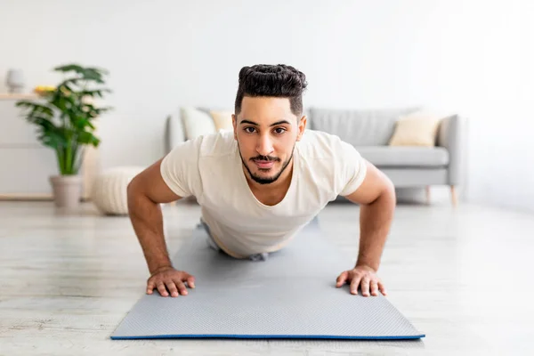 Hombre árabe joven fuerte haciendo ejercicio de fuerza, de pie en la pose tablón en casa — Foto de Stock