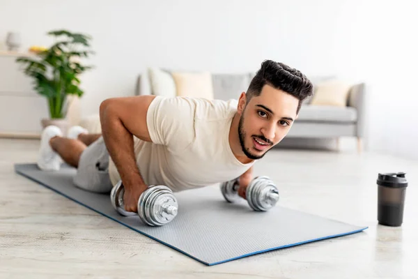 Bleiben Sie zu Hause fit. Starker junger arabischer Mann beim Ganzkörpertraining, in Plankenpose stehend, mit Hanteln drinnen — Stockfoto