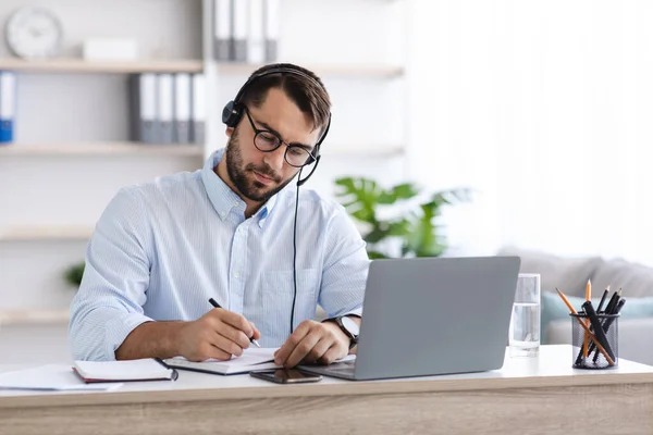 Ocupado hombre europeo de mediana edad con barba en gafas, auriculares trabajando en el ordenador portátil —  Fotos de Stock