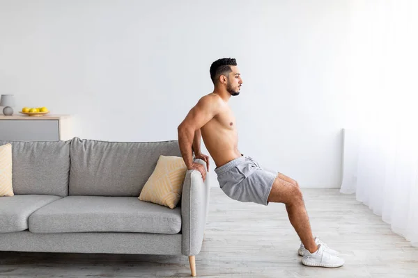 Gesund leben. Sportlicher junger Araber macht Kraftübungen in der Nähe des heimischen Sofas, kopiert Raum — Stockfoto
