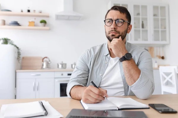 Pensif adulte caucasien gars enseignant ou homme d'affaires avec barbe dans des lunettes prend des notes, fonctionne à l'ordinateur portable — Photo