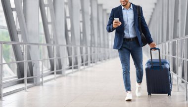 Havaalanında bavulla yürürken akıllı telefon kullanan tanınmayan genç iş adamı.