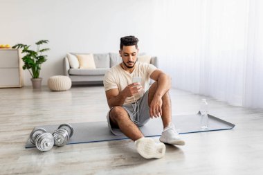 Ev içi spor eğitiminden sonra kulaklıkları ve cep telefonu olan çekici genç bir Arap müzik dinliyor.