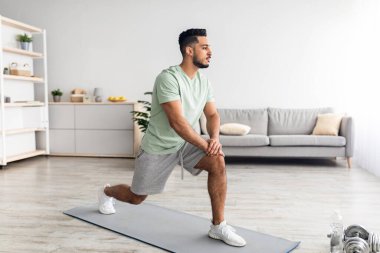 Formda genç bir Arap hamlesini yapıyor, güç egzersizleri yapıyor, evde bacak kaslarını çalıştırıyor, uzun boylu.