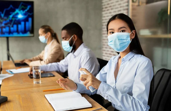 Empresária asiática usando máscara médica aplicando spray desinfetante durante reunião corporativa — Fotografia de Stock