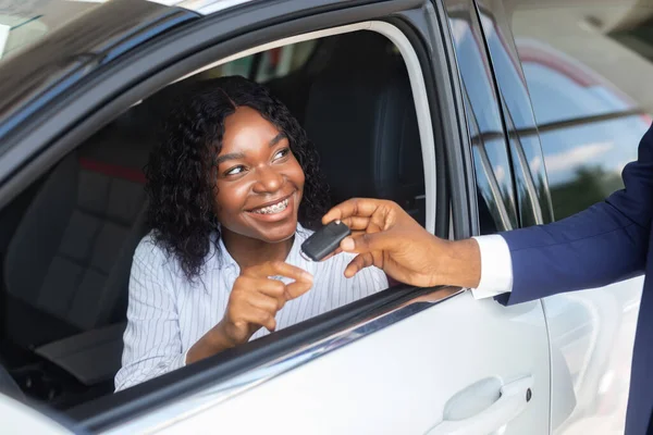 Negro mujer sentado en coche y tomando clave de vendedor en Showroom — Foto de Stock