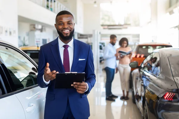 Autókereskedés. Jóképű fekete menedzser pózol a munkahelyen az Auto bemutatóteremben — Stock Fotó