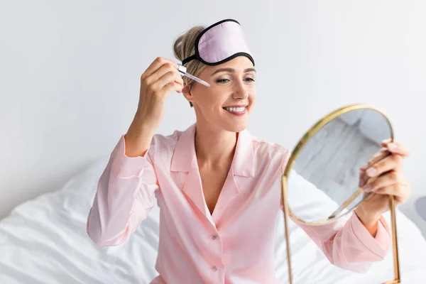 Porträtt av leende kvinna hålla spegel tillämpa viktigt serum — Stockfoto
