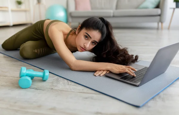 Ung indisk kvinna känner sig trött, liggande på yogamatta framför laptop, för utmattad för att börja online träning hemma — Stockfoto