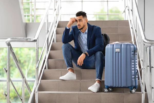 Cancelación de vuelo. Hombre árabe trastornado sentado con equipaje en las escaleras en el aeropuerto — Foto de Stock