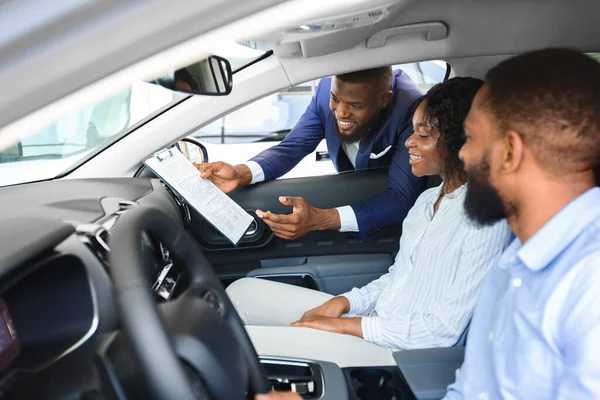 Giovane coppia nera seduta all'interno di una nuova auto nello showroom, venditore professionista di ascolto — Foto Stock