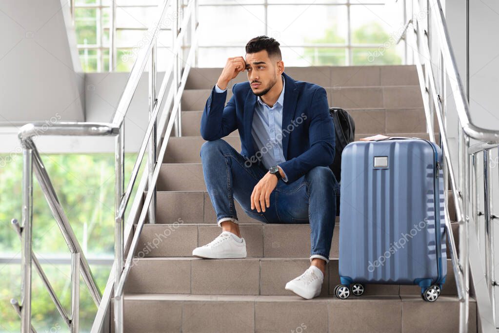 Flight Cancellation. Upset Arab Man Sitting With Luggage At Stairs In Airport