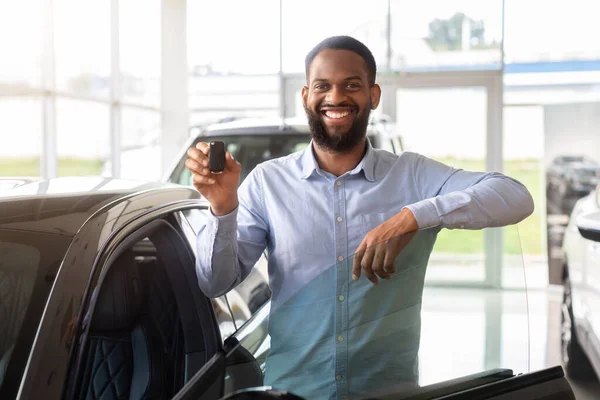 Χαρούμενος ιδιοκτήτης. Χαρούμενος μαύρος άνδρας στέκεται κοντά στο νέο αυτοκίνητο και κρατώντας τα κλειδιά — Φωτογραφία Αρχείου
