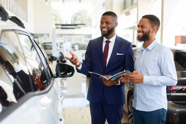 Black Salesman Advertising New Automobile To Male Customer In Car Dealership Center — Stock Photo, Image