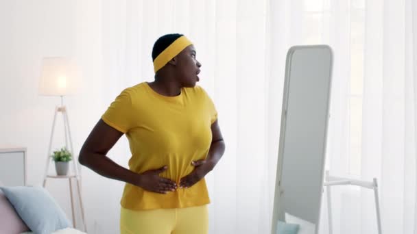 Mujer negra con sobrepeso feliz mirando el espejo en casa, disfrutando del resultado de la dieta — Vídeos de Stock