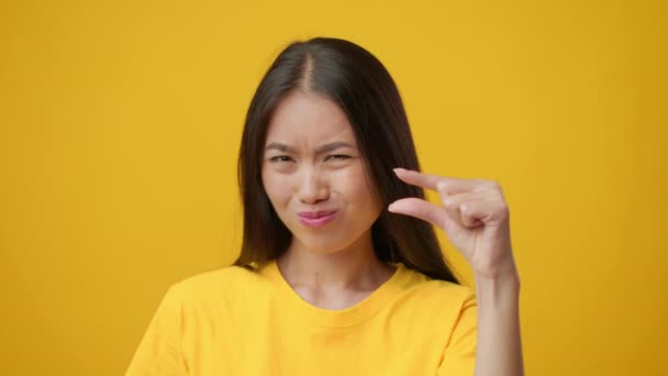 指で小さなサイズのジェスチャーを示す日本人女性,黄色の背景 — ストック動画