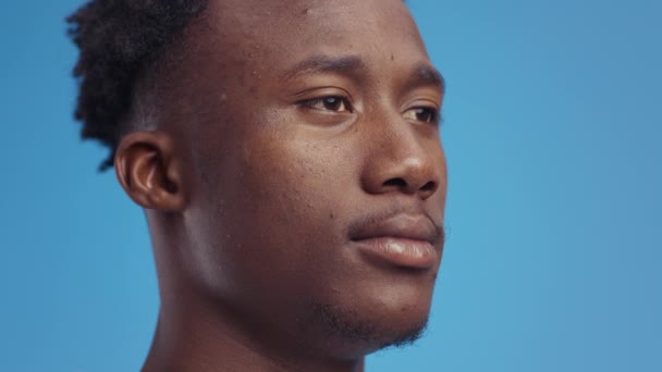 Semi profiel portret van jonge zelfverzekerde serieuze Afrikaanse Amerikaanse man op zoek opzij, blauwe studio achtergrond, vrije ruimte — Stockvideo