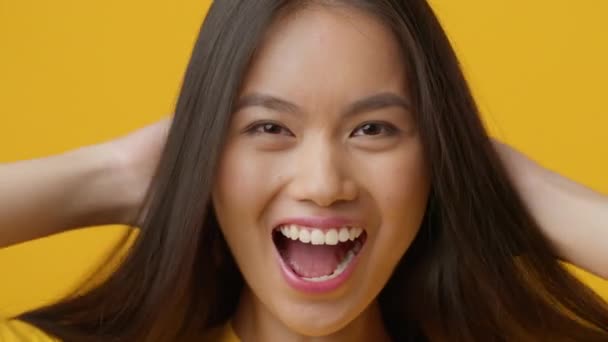 Emocionado asiático hembra jugando con largo pelo sobre amarillo fondo — Vídeo de stock