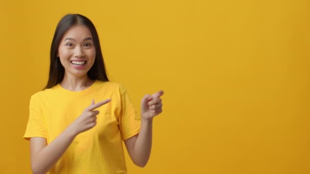 Emocionada mujer china señalando dedos aparte de los pulgares gestos hacia arriba, fondo amarillo — Vídeo de stock