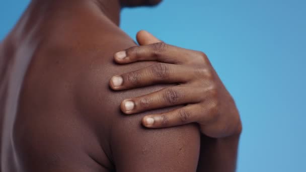Irreconocible afroamericano hombre masajeando su hombro desnudo inflamado, que sufre de dolor muscular, fondo azul — Vídeo de stock
