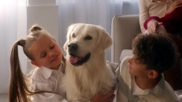 Veselé děti mazlící se pes sedí na podlaze doma — Stock video