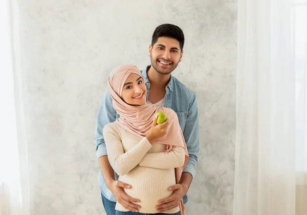 Estilo de vida saludable durante el embarazo. Amoroso árabe casado pareja abrazos, embarazada esposa comer manzana — Foto de Stock