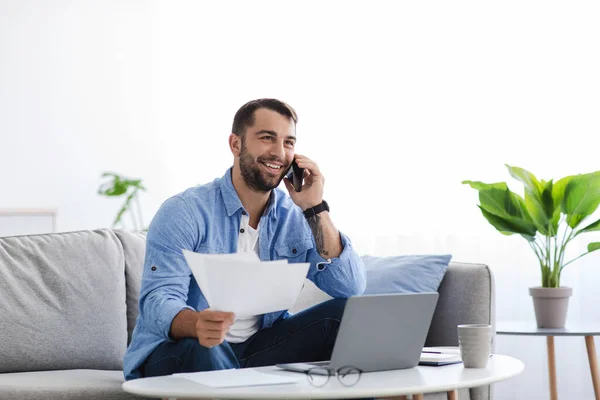 Occupé souriant adulte européen assis sur le canapé travailler à la maison avec des documents, parler avec le client par téléphone — Photo