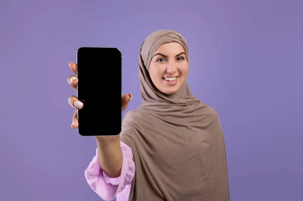 Gambar mockup smartphone dengan layar hitam kosong di tangan wanita muslim yang bahagia dalam jilbab, fokus selektif — Stok Foto