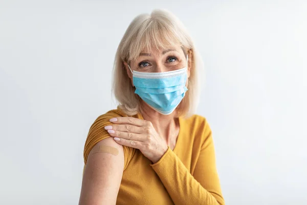 Vaccineerde volwassen vrouw dragen gezicht masker poseren over grijze achtergrond — Stockfoto
