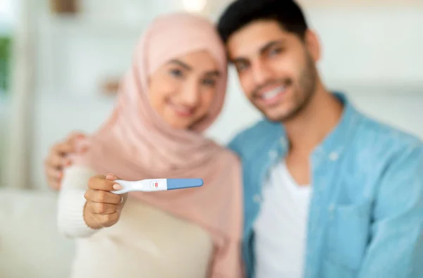 Primer plano de la prueba de embarazo positiva en las manos de la mujer musulmana abrazándose con su marido y sonriendo a la cámara — Foto de Stock