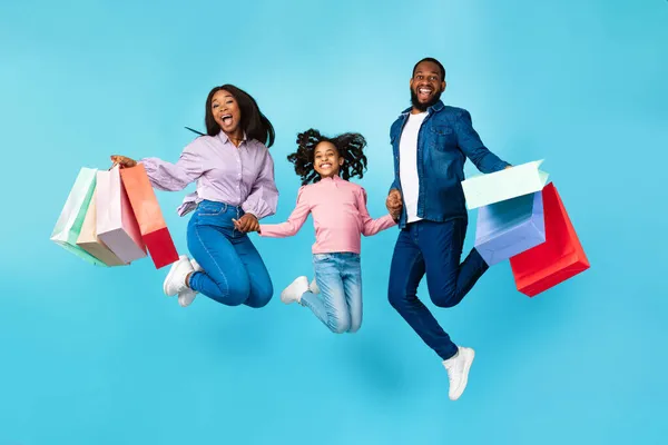 Aufgeregte, fröhliche schwarze Menschen springen und halten Einkaufstüten in der Hand — Stockfoto