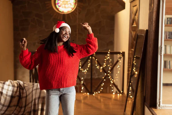 Bella signora nera che balla con la musica preferita, indossa cappello e maglione di Babbo Natale, si diverte a Natale a casa, spazio libero — Foto Stock