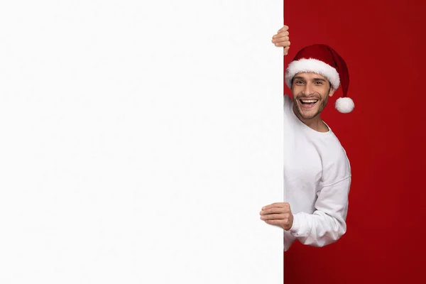 Weihnachtsangebot. Fröhlicher Millennial-Mann mit Weihnachtsmütze und weißer Werbetafel — Stockfoto