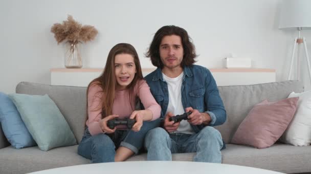 Joven hombre y mujer emocional jugando juegos con joystick, dama disfrutando de la victoria y abrazando a su novio molesto — Vídeo de stock