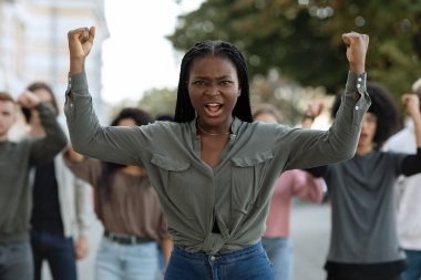 Siyahi kadın çok ırklı aktivistlere rehberlik ediyor, yumruklarını kaldırıyor.