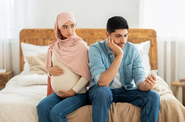 Young pregnant muslim woman offended to her husband busy with smartphone, arab lady in hijab feeling lonely — ストック写真