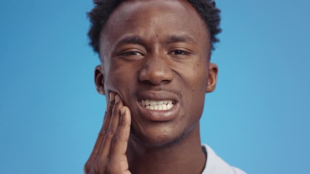 ปัญหาสุขภาพฟัน ชายหนุ่มชาวแอฟริกันอเมริกัน นวดขากรรไกรที่เจ็บปวด ทรมานจากอาการปวดฟัน พื้นหลังสีฟ้า — วีดีโอสต็อก