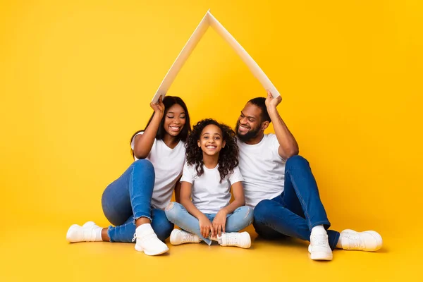 Pais afro-americanos felizes segurando telhado de papelão acima da filha — Fotografia de Stock