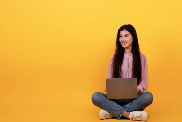 Boldog örmény nő használ laptop számítógép sárga stúdió háttér, ül a padlón, és nézi a másolás tér — Stock Fotó