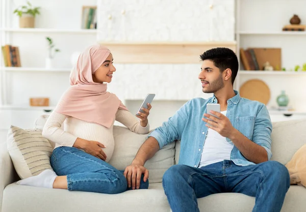 Emberek és technológia koncepció. Boldog muszlim terhes házastársak pihen okostelefonok és beszélgetnek egymással — Stock Fotó
