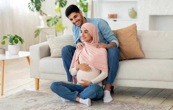 Zwangere moslimvrouw voelt zich ontspannen, zit op de vloer in de woonkamer en attente echtgenoot masseert haar schouders — Stockfoto