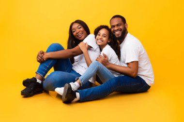 Afro-Amerikalı bir adam karısını kucaklıyor ve gülümsüyor.