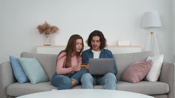 Rodzinne zakupy online. Młody mężczyzna i kobieta dokonują zakupów w internecie, siedząc na kanapie z laptopem i kartą kredytową — Wideo stockowe