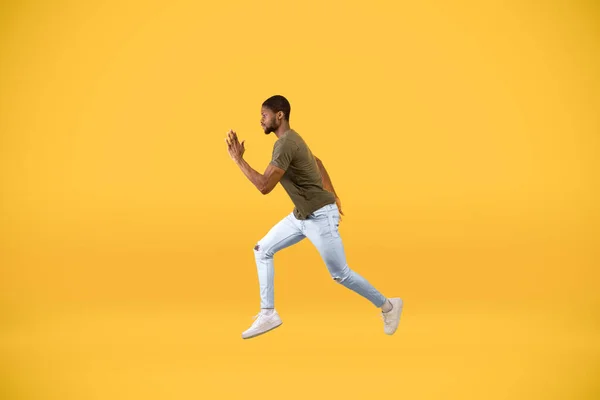 Joven afroamericano hombre corriendo sobre amarillo estudio fondo, en movimiento vista lateral disparo de chico saltando en el aire —  Fotos de Stock