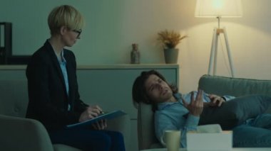 Bunalımlı bir adam, kişisel görüşmeler sırasında sorunları hakkında konuşuyor, kanepeye uzanıyor, psikolog notlar yazıyor.