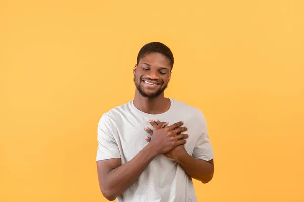 Cordialissimo ragazzo nero che tiene le mani sul petto, esprimendo gratitudine ed emozioni positive, sfondo giallo — Foto Stock